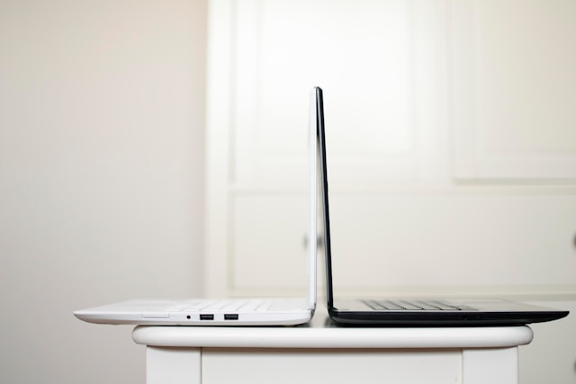 A white laptop and a black laptop on a white table.

