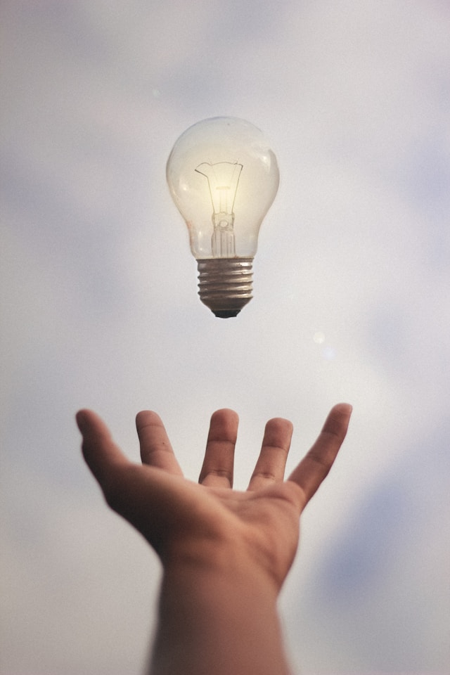 An incandescent light bulb levitates above an outstretched hand.