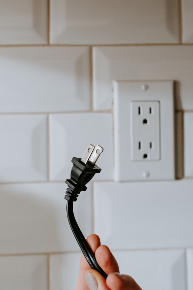Une personne tient un câble noir avec une fiche de type A à une extrémité près d'une prise électrique.
