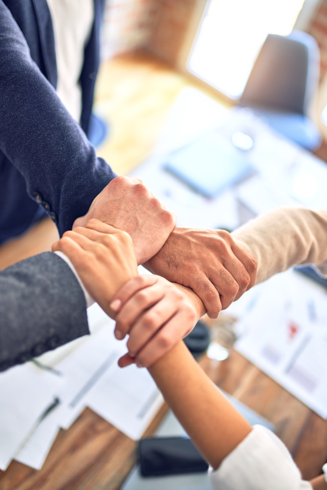 Four people hold hands above a table.
