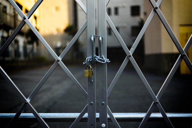 A closeup of a gray gate with a chain and a golden padlock.
