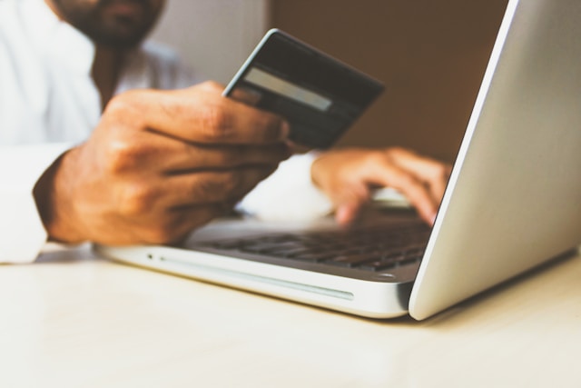 A person with a white shirt holds a debit card and enters the card details on a laptop.