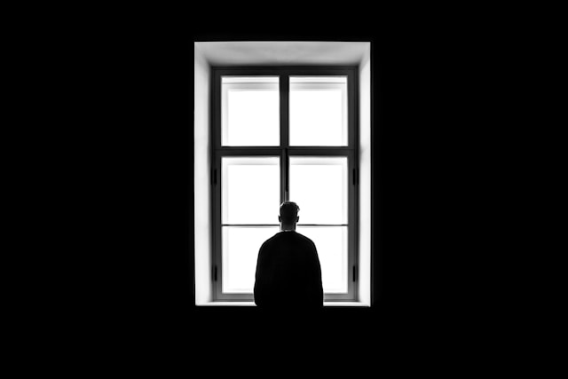 A person stands in front of a window and looks outside.