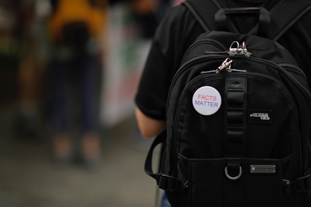 A white badge with the text “Facts Matter” in pink and purple on a black bag. 