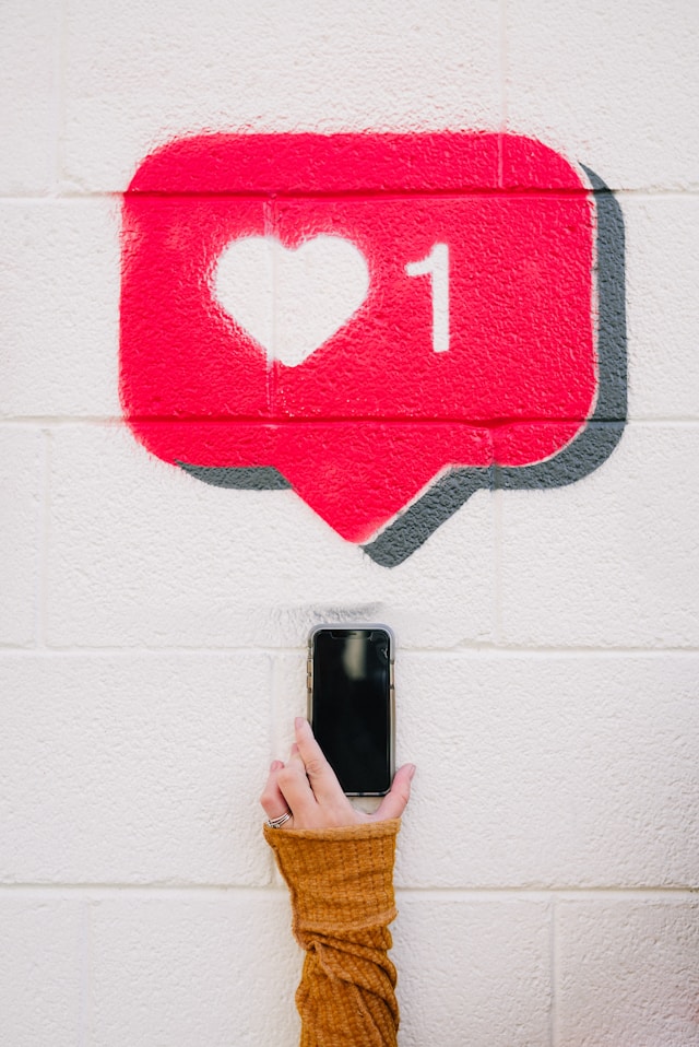 A person holds an iPhone under a red chat bubble with a heart and the number one.