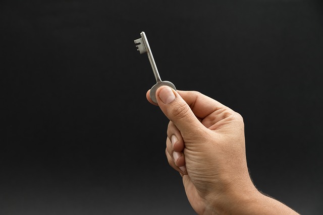 Een persoon houdt een grijze metalen sleutel tegen een donkere achtergrond.