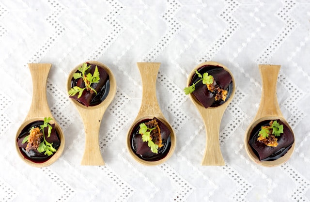 Five chocolate cakes with melted chocolate on light brown wooden spoons on a white surface.