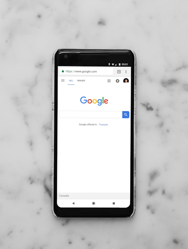 黒いスマートフォンのモバイルブラウザに表示されるGoogle検索のホームページ。
