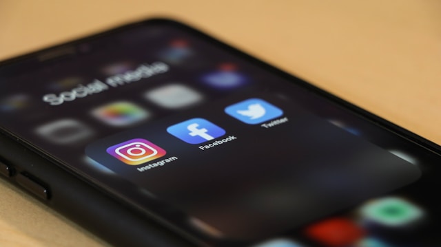 Uma pasta com as aplicações Instagram, Facebook e Twitter num iPhone preto.