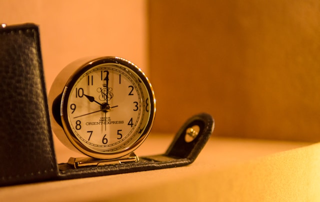 A closeup of a clock with a classic design on a shelf.
