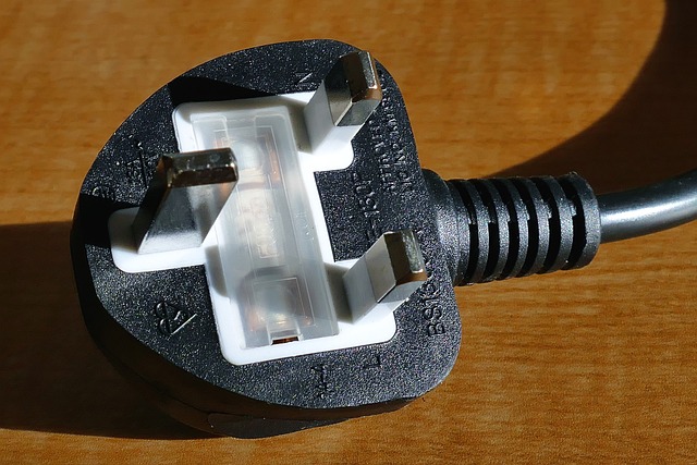 A closeup of a three-pin black electrical plug on a brown wooden surface.