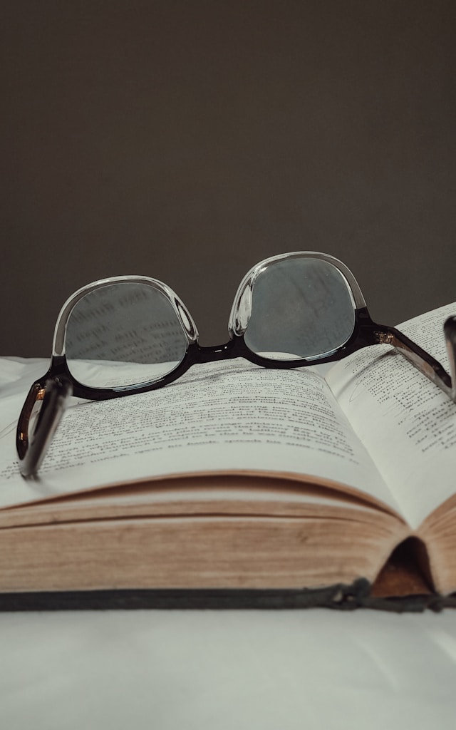 Sepasang kacamata dengan bingkai hitam di atas buku yang terbuka.