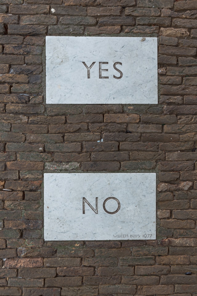 오래된 벽돌 벽에 "예"와 "아니오"가 적힌 흰색 표지판 두 개가 있습니다.