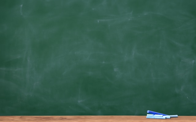 A close-up of a green chalkboard with multiple pieces of blue chalk under it.