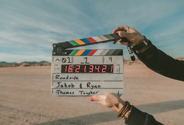 A person with black sleeves holds a clapperboard and a black marker.