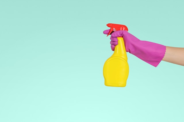 A person with a purple glove holds a yellow and red pump spray bottle.
