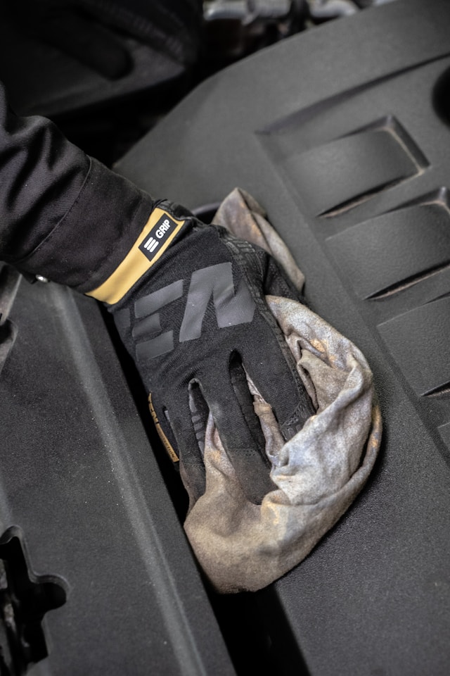 Een persoon draagt zwarte handschoenen en veegt een donker oppervlak af met een vuil stuk stof.
