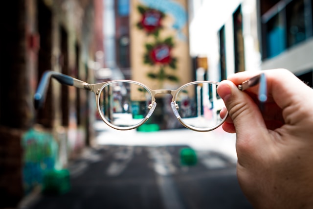 A person holds a pair of glasses with a rose gold and black frame.