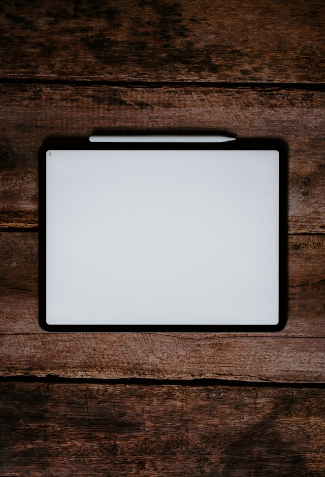 Una pantalla blanca en un iPad negro con un lápiz Apple blanco sobre una superficie de madera marrón.