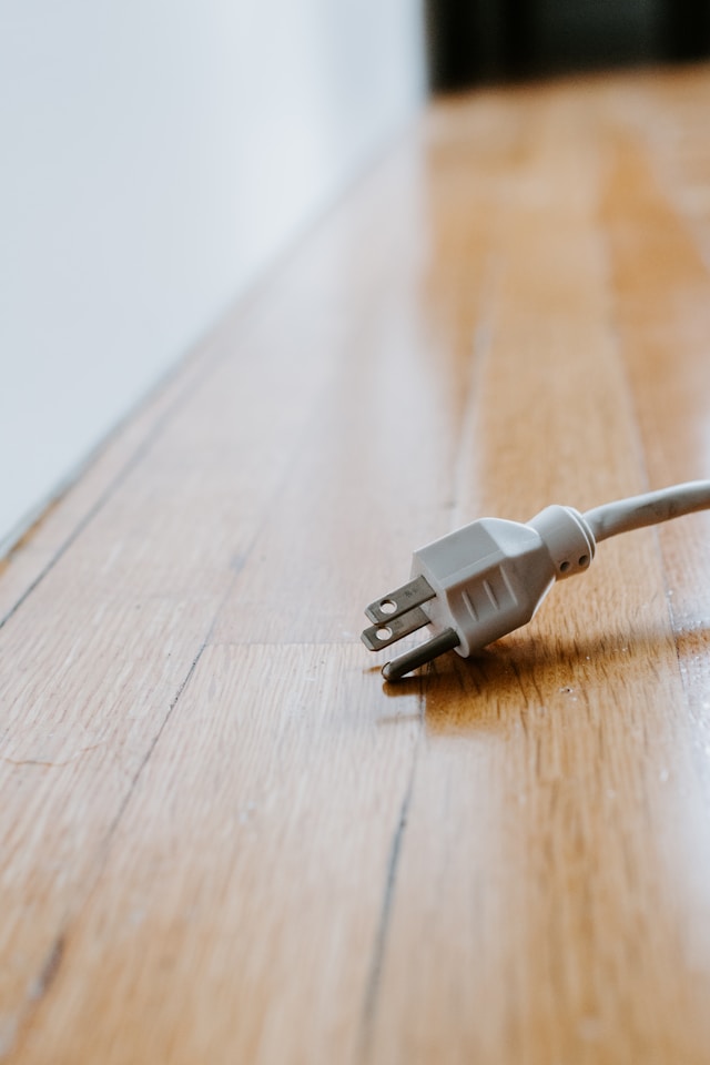 Een witte kabel met drie pinnen op een bruine houten vloer.
