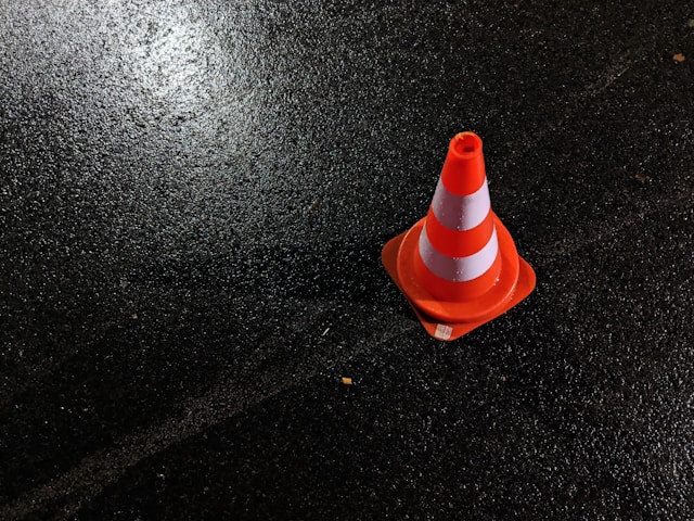 A closeup of an orange cone with white stripes on the road.
