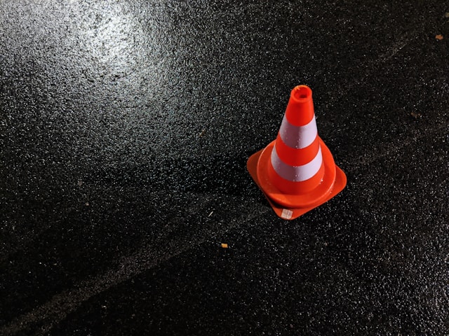 Primer plano de un cono naranja con rayas blancas en la carretera.
