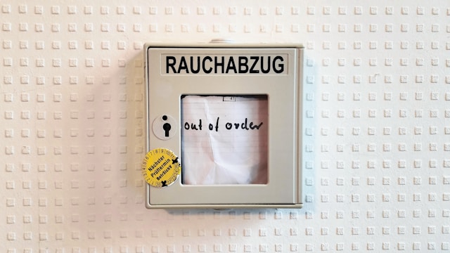 A beige German smoke outlet on a white wall with multiple square prints indicates it is out of order.