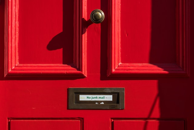 Bidikan close-up pintu merah dengan frasa "tidak ada surat sampah" pada kotak suratnya.