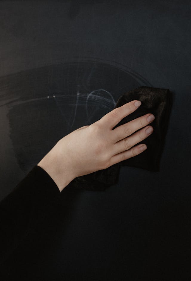 A person uses a black cloth to wipe a chalkboard.