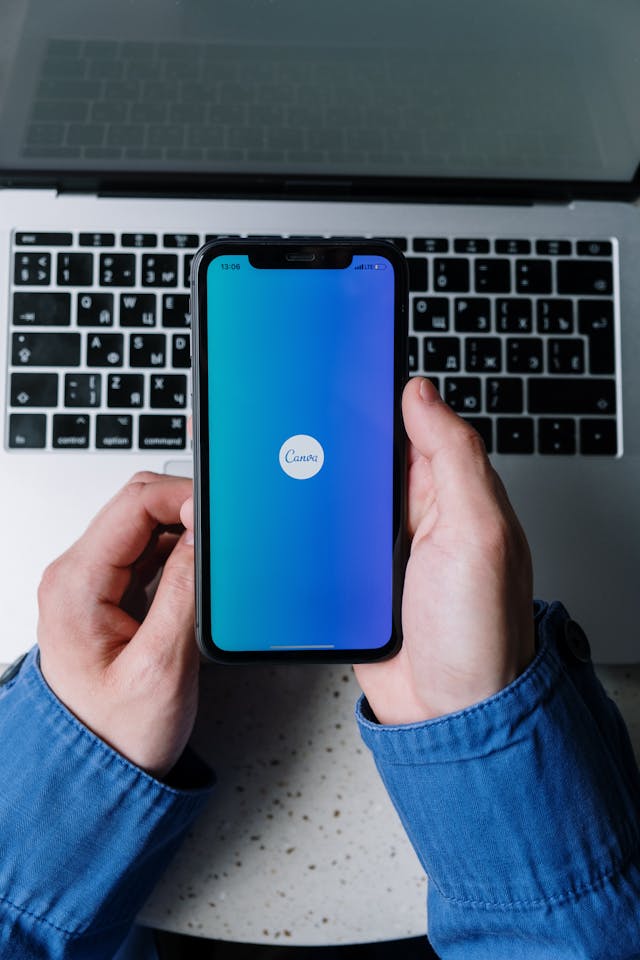 Una persona con mangas azules abre la aplicación Canva en su iPhone negro.
