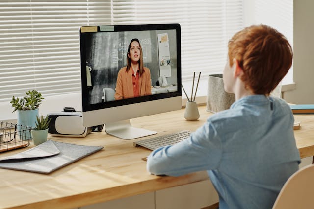 Een kind zit en volgt een virtuele les op een iMac.