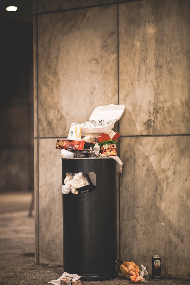 Un cubo de basura negro lleno de basura.
