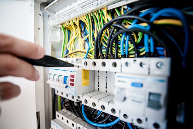 Un electrician folosește o șurubelniță pentru a deșuruba un întrerupător de circuit dintr-un tablou de distribuție.