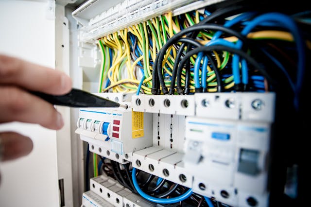 An electrician uses a screwdriver to unscrew a circuit breaker from a switchboard.