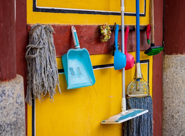 Pe un perete maro și galben sunt atârnate mai multe echipamente pentru curățarea unei gospodării.