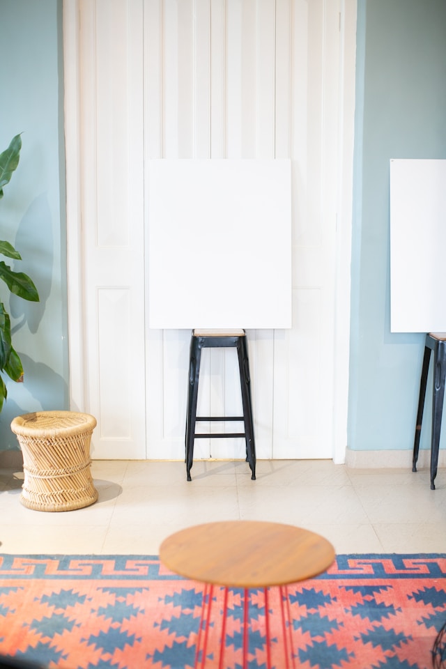 Une toile blanche sur un tabouret noir dans une pièce avec une porte blanche et des murs bleu clair.
