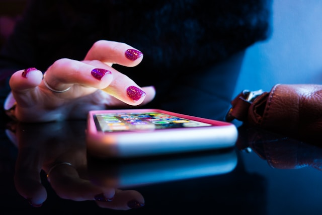 Uma pessoa com verniz vermelho nas unhas utiliza um iPhone com uma capa cor-de-rosa.
