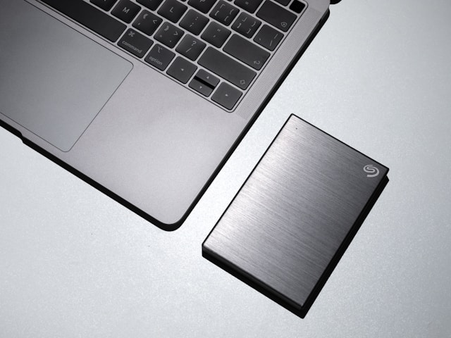 Um MacBook cinzento junto a uma unidade externa de estado sólido Seagate cinzenta.
