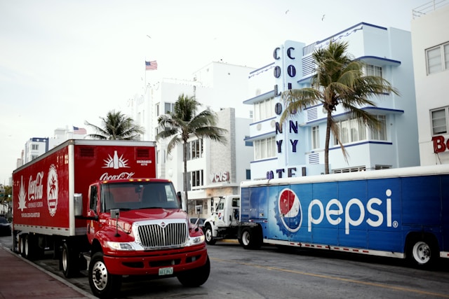 파란색과 흰색 펩시 트럭의 반대편에 빨간색 코카콜라 트럭이 있습니다.