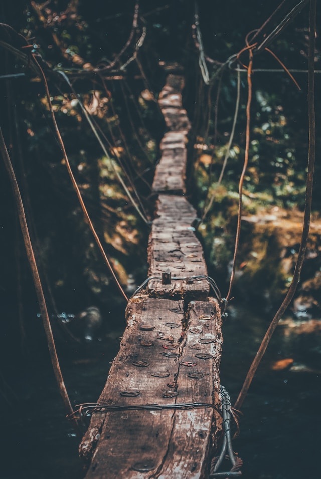 Foto close-up jembatan gantung kayu dengan jalan setapak yang sempit.
