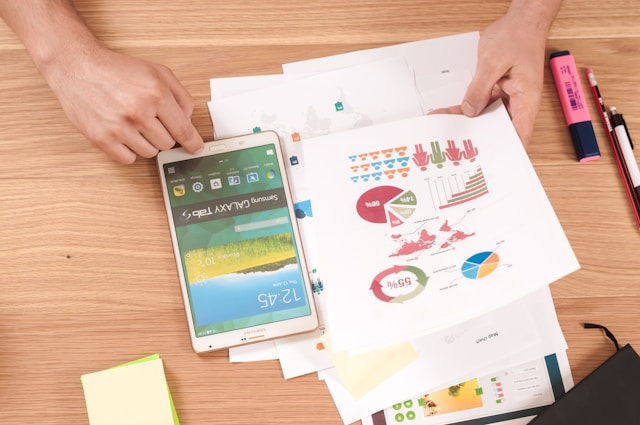 A person holds a piece of paper with graphs and uses a white Samsung Galaxy Tab S.