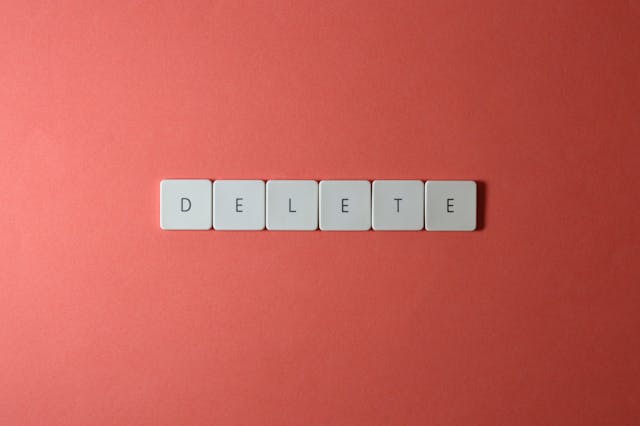 アースカラーの赤を背景に、白いキーボードのようなタイルに描かれた「delete」の文字。