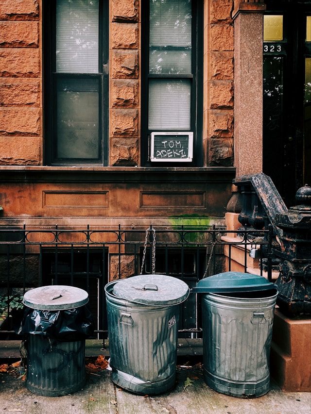 Tres cubos de basura grises junto a una barandilla negra.