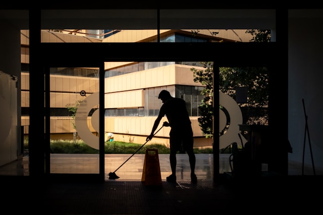 Het silhouet van een man met een dweil bij de ingang van een gebouw.