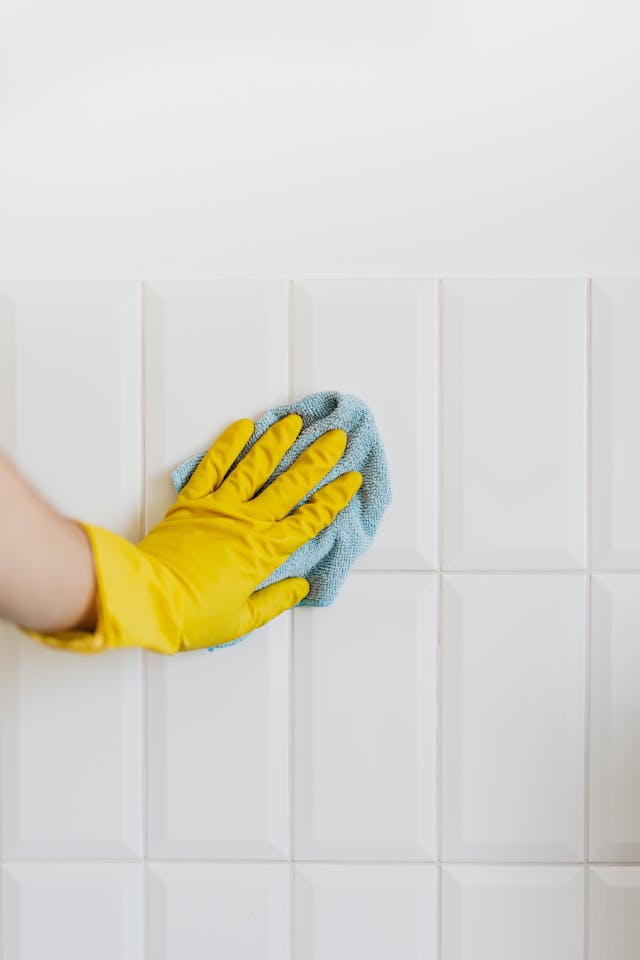 A person with a yellow glove uses a blue cloth to wipe a white wall.