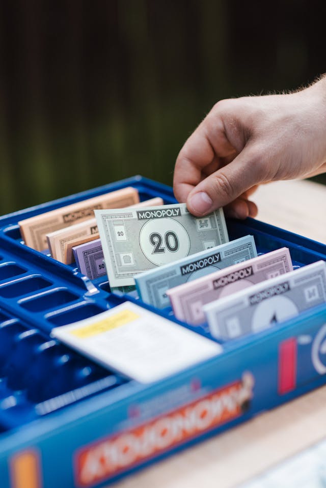 Une personne choisit un faux billet de banque vert dans une boîte de Monopoly bleue.