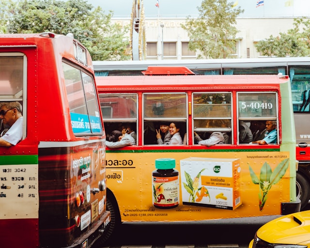 Two red buses with advertisements in traffic.