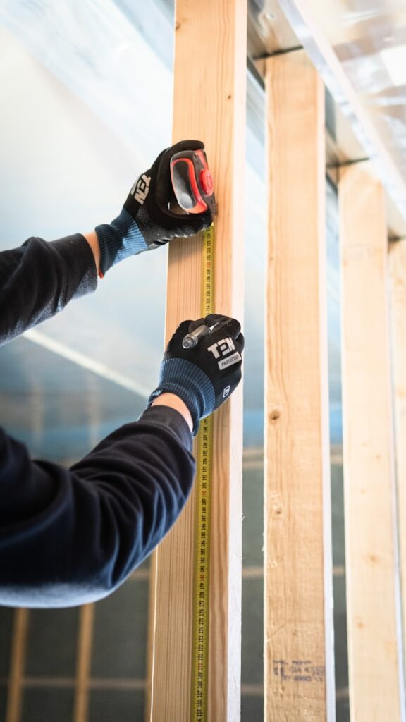 Eine Person benutzt ein Maßband an einem Holzbalken.