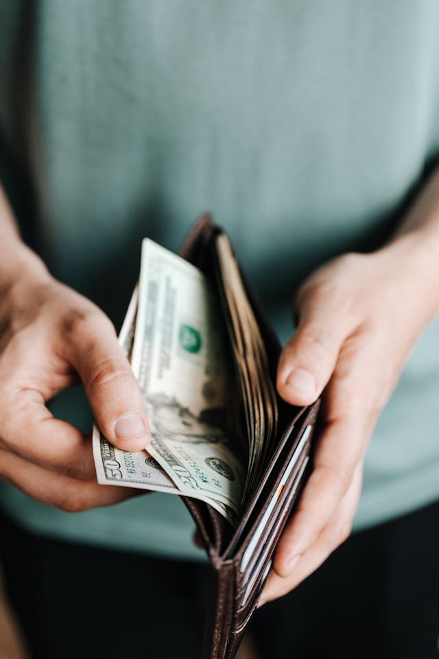 A person with a green shirt pulls out a $50 and $20 note from their brown wallet.