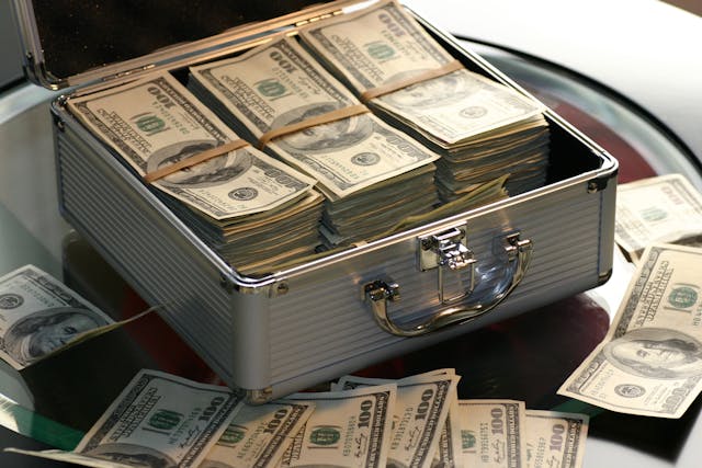 A silver briefcase with multiple hundred U.S. dollar banknotes on a glass table.